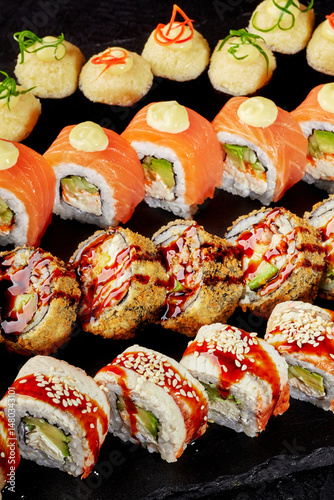 Sushi set displayed on black stone featuring variety of rolls and toppings