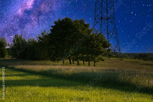 Stunning nightscape with a shooting star and Milky Way over a tranquil field, framed by trees and power lines, capturing the serene beauty of the cosmos