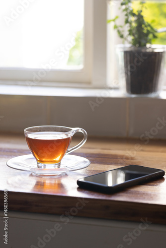 Wallpaper Mural glass teacup resting on saucer on countertop near potted plant and smartphone, sunlight filtering Torontodigital.ca