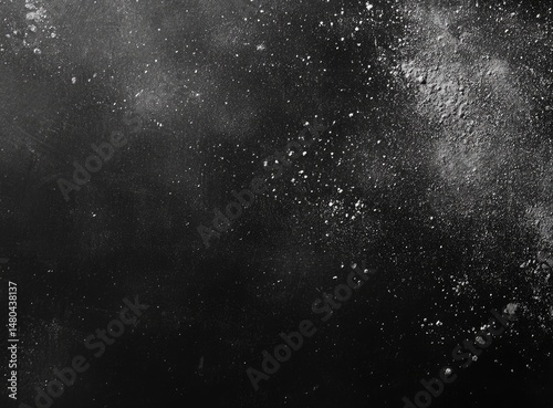 Dark surface dusted with light particles.  Fine, light gray powder scattered unevenly across a dark backdrop