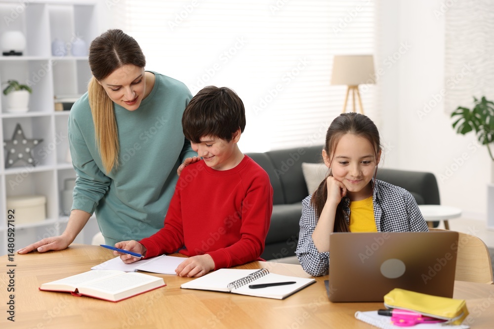 Mother helping her kids with homework at wooden table indoors Mother helping her kids with homework at wooden table indoors