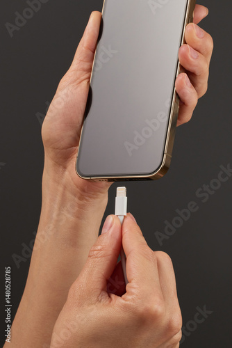 female hand plugging charger cord into smartphone to charge battery on black background, Wired charging