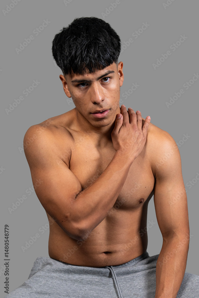 Shirtless latino man touching shoulder posing in studio Shirtless latino man touching shoulder posing in studio