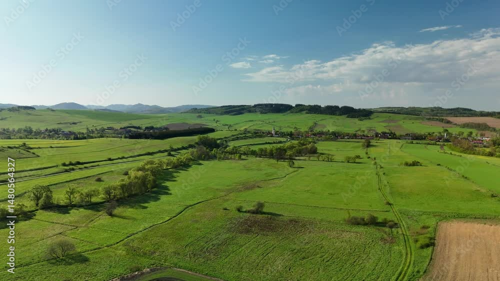 Aerial view of a scenic rural landscape with green hills, farmland, and a peaceful village surrounded by nature and open fields.