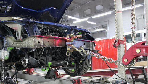 Damaged Car Suspended by Chains on Frame Straightening Rack in Automotive Workshop. Auto Body Frame Machine at Works in Car Service Station
