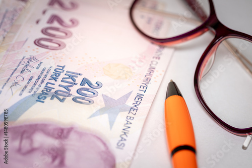 Fototapeta Naklejka Na Ścianę i Meble -  Turkish lira money on the desk next to women's glasses, white sheet of paper and pen, concept, payment of bills, installments and loans, rising costs of household budget in Turkey