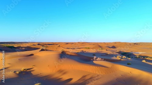 Drone flyover of sand dunes at sunrise or sunset. Soft light, smooth desert shapes, and clear sky create a serene and tranquil mood.