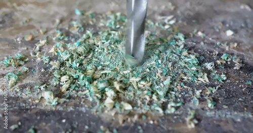 Drill bit piercing through material creating green dust