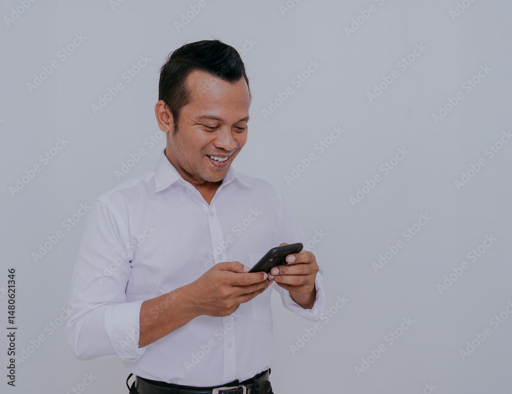 Asian man wearing white shirt smiling looking to his mobile phone screen isolated on white background. Asian man wearing white shirt smiling looking to his mobile phone screen isolated on white background.