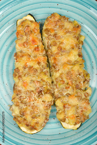 Two halves of baked stuffed zucchini with melted cheese are presented on a light blue plate
