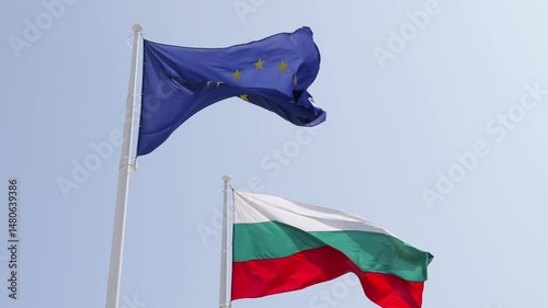 Slow motion - the flags of the European Union and Bulgaria waving in the wind against a blue sky. Summer day, sunlight. Concept of freedom, politics, patriotism, diplomacy and international relations.