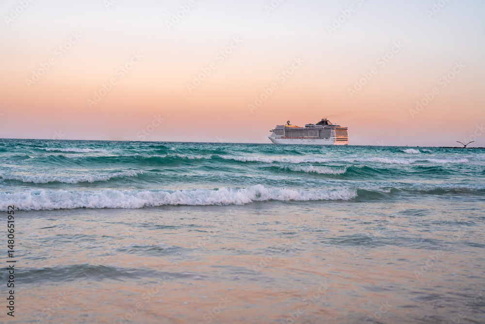 Obraz premium Cruise ship on the ocean. Luxury liner at sea. Miami Beach with cruise ship. Sea water and cruise liner. Tourist cruise ship near coast. Ocean waves and vessel boat. Summer dream vacation. Boat trip.