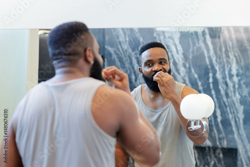 Flossing mid-age African American man wearing tank top at bathroom sink, with mirror and floss