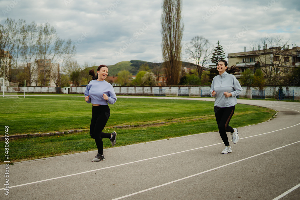 Fototapeta premium Two female friends running or jogging on stadium doing sport activities