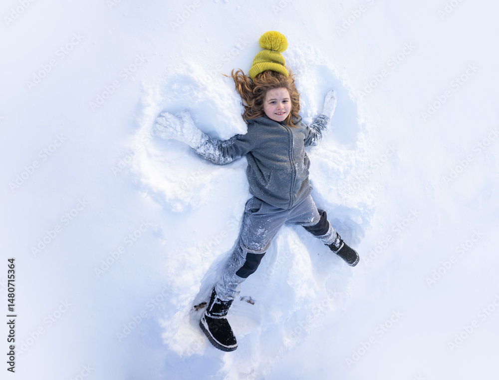 Fototapeta premium Winter fun. Child making a snow angel in winter day. Happy kid lying in the snow. Kid angel in snow. Winter kids with snowy angel wings. Smiling child on a winter day. Child in the snow lake angel.