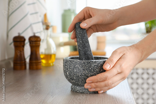 Fototapeta Naklejka Na Ścianę i Meble -  Woman with mortar and pestle at wooden table in kitchen, closeup