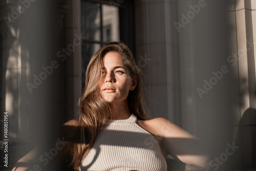 Woman Portrait Sun Light Window - Young woman in a white top posing for a portrait in front of a window with sunlight streaming through.