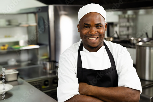 African American chef smiling in professional kitchen, wearing chef's hat and black apron photo