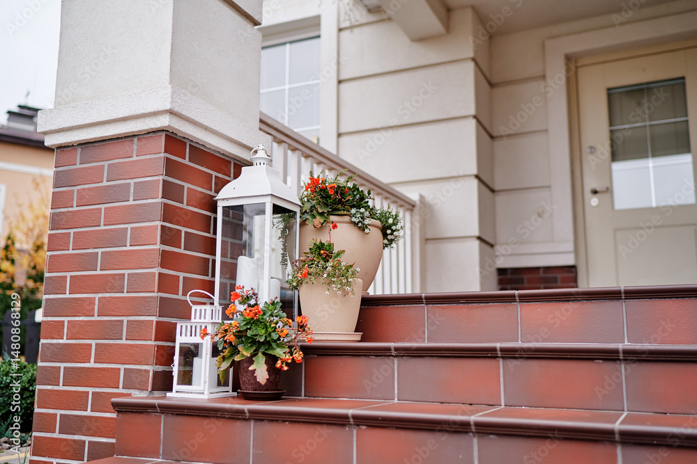 Fototapeta premium Elegant Front Porch Decor with Flowers and Lanterns on Brick Steps..
