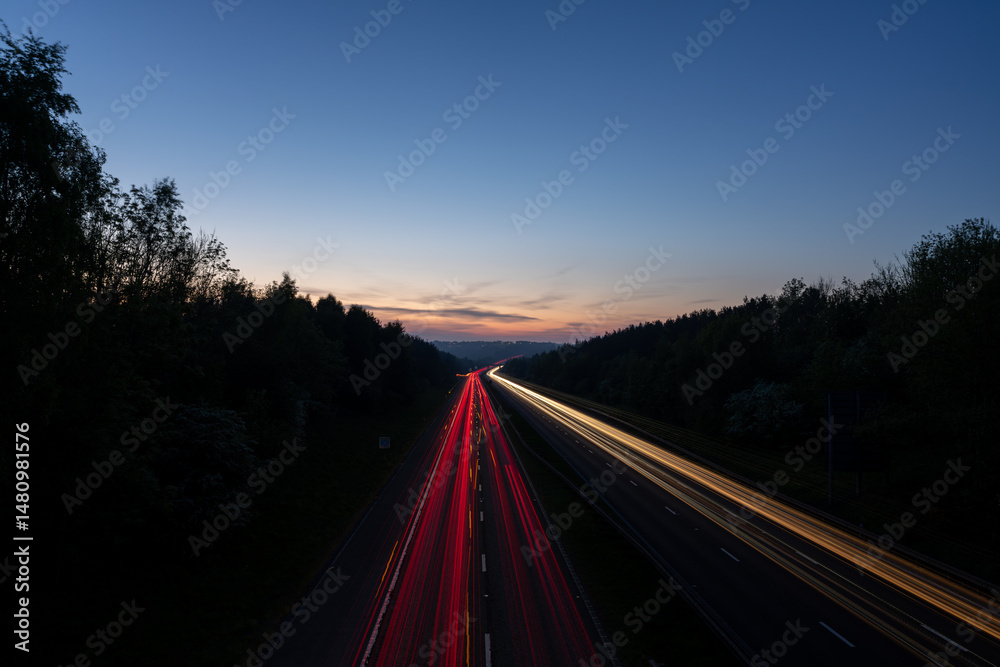 Fototapeta premium Light trails illuminating highway at dusk with forest on both sides