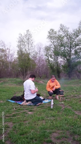 couple and their dog on picnic , cooking meat sausages on camping stove