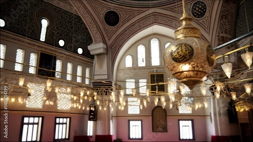 Ornate golden lamp with Arabic script hanging in a spacious religious building with windows and arched ceiling.