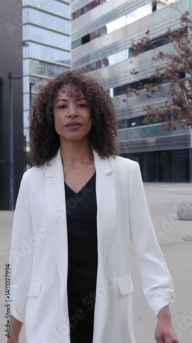 Vertical. Empowered African business woman walks confident out of office and looks diverse co-workers. Elegant young adult successful formal female entrepreneur strolls outside city financial centre