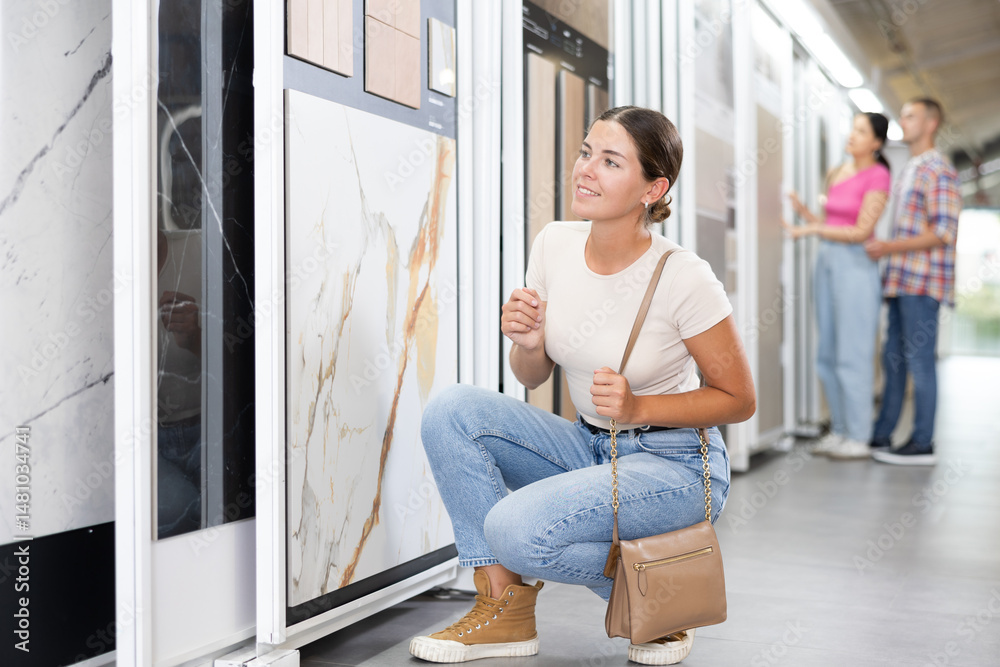Young woman customer selects ceramic tiles from samples in hardware store
