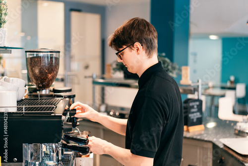Young barista making coffee at automatic machine in a modern coffee shop. Student working part-time in cafe. Problems of unemployment and Job opportunities for youth. Small business vacancies