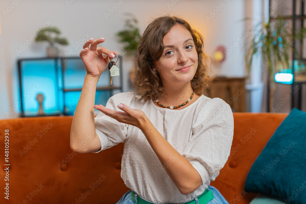 Happy young woman real estate agent lifting hand showing the keys of new home house apartment, buying or renting property, mortgage loan at home indoors. Girl sitting on orange sofa couch. Lifestyles. Happy young woman real estate agent lifting hand showing the keys of new home house apartment, buying or renting property, mortgage loan at home indoors. Girl sitting on orange sofa couch. Lifestyles.