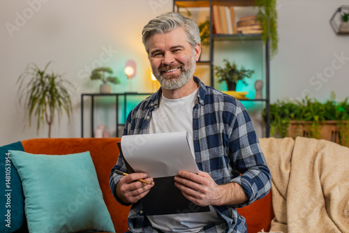 Foto Smiling bearded mature man in casual clothes with documents analyzing information reading business papers prepare financial report