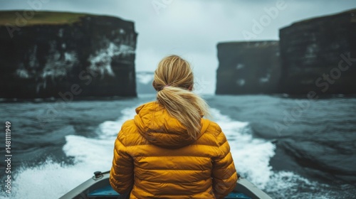 Woman in yellow jacket on a boat sailing between dramatic sea cliffs