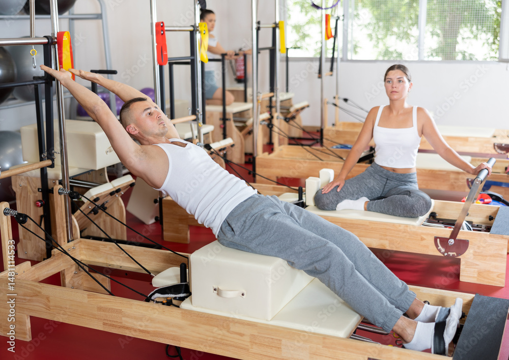Young athletic man training his abs on pilates reformer in pilates studio