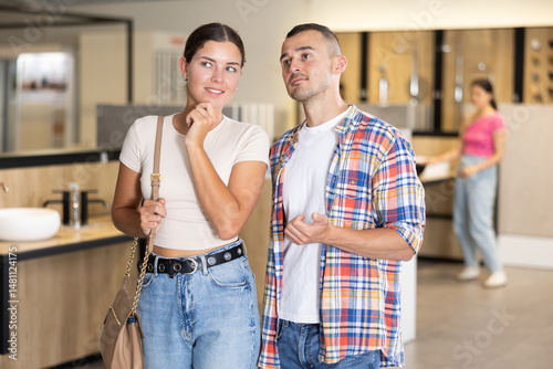 Obraz na płótnie Positive friendly young couple looking with interest for bathroom decor and fixtures in showroom, evaluating different options for home improvement .. w salonie