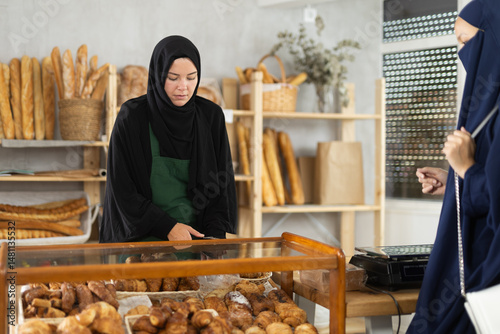 Obraz na płótnie Focused young Muslim woman of European appearance wearing black hijab working in cozy small bakery, arranging freshly baked pastries on display w salonie