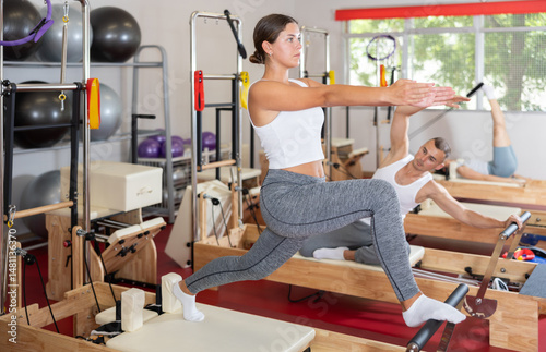 Obraz na płótnie Sportive young girl training her arms and legs on reformer machine in fitness hall w salonie