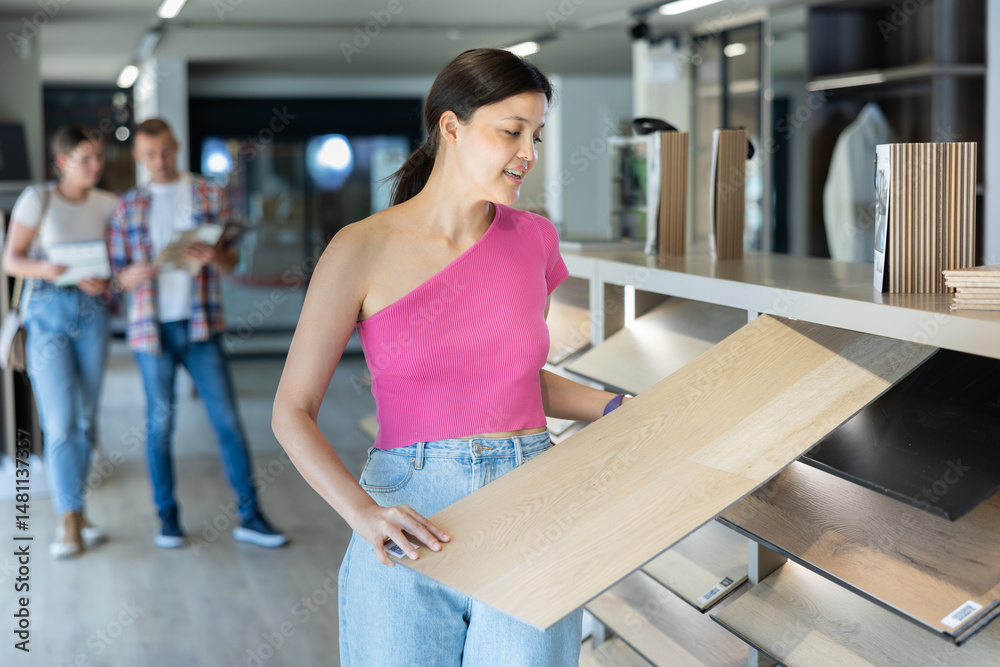 Young woman buyer chooses sample of laminate flooring in hardware store