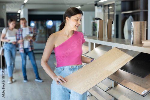 Young woman buyer chooses sample of laminate flooring in hardware store