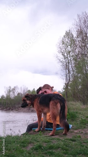 couple with their dog sitting in the forest by the river enjoying nature hugging pet