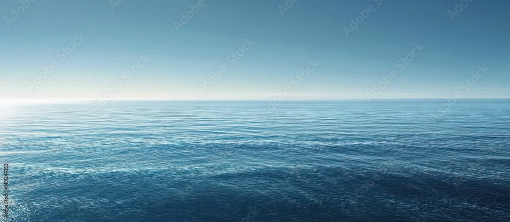 Obraz premium Calm expansive ocean under clear blue sky with gentle waves and bright sunlight on water surface creating peaceful atmosphere