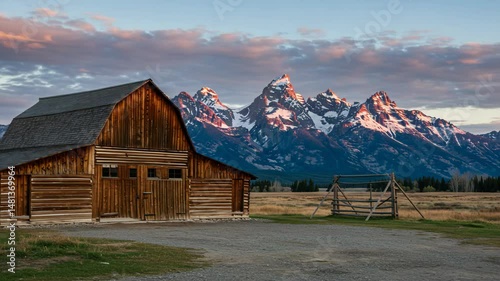 Rustic barn nestled against snow-capped mountains at sunset with soft light.