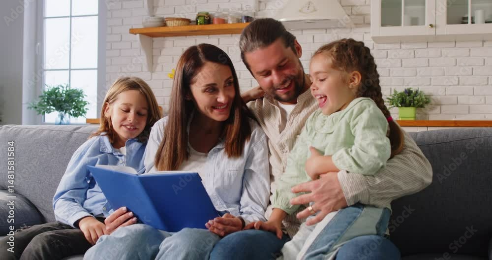 Full family gathered together on sofa in living room, reading book to children, taking care of education development, enjoying leisure time at home. Parents reading fairy tales to som and daughter
