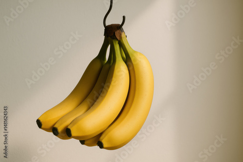 Bunch of ripe yellow bananas hanging on hook with soft natural light creating calm and fresh atmosphere in image