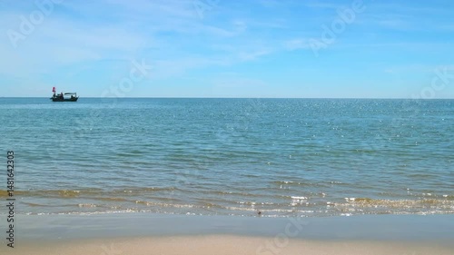 The atmosphere of the sea in the morning with blue sky, green sea and waves hitting the sandy beach. In the sea there are small fishing boats playing.