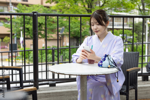 カフェのテラス席でスマートフォンを操作する着物を着た若い日本人女性 photo