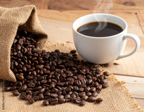 Kenyan coffee beans roasted dark, arranged in a rustic setup beside a steaming cup of fresh coffee. photo