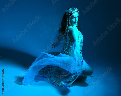 Fantasy studio portrait of a red-haired mermaid faery model wearing white pearl gown, fairytale costume. classical sitting pose,, ethereal moody blue lighting as if underwater on studio background