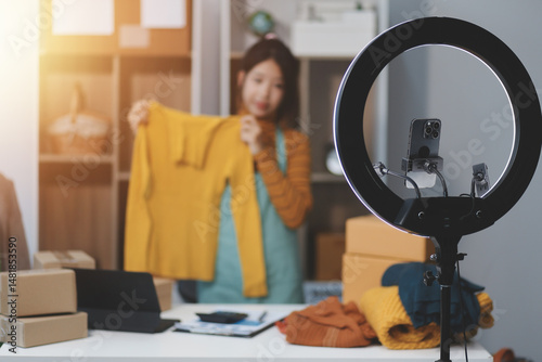vlogger, blogger small SME business asian beautiful woman using mobile phone video call for sell clothes live stream selling online, show product present detail at home office, entrepreneur ecommerce