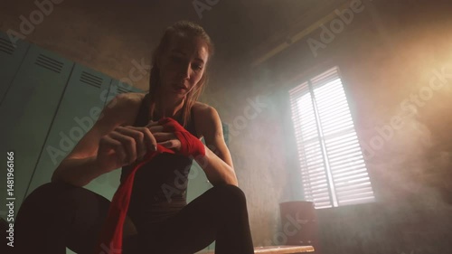 Athletic woman wrapping hands by red elastic tape in changing room of sport hall . Be strong and sportive, practicing box for self-defense and losing weight, sport for stay slender and keep fit