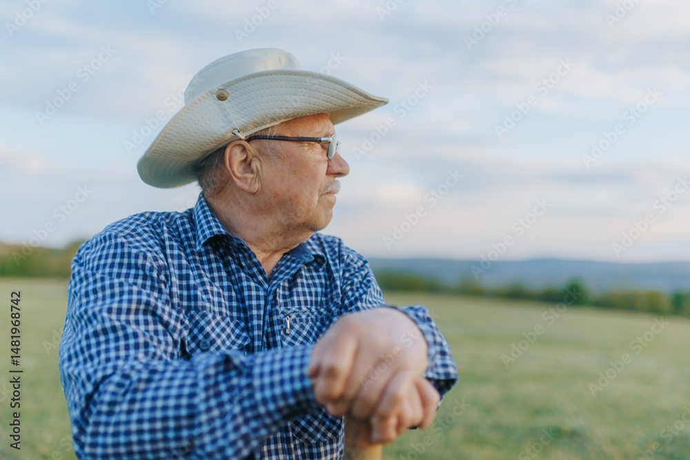 Fototapeta premium Elderly Cowboy Farmer Stands Still as Sunset Falls on the Farmland